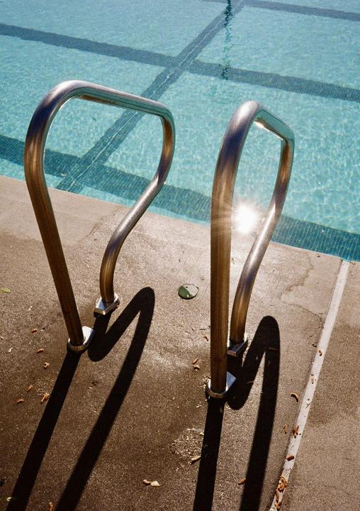 Sunlight reflects off the metal handrails of a swimming pool.