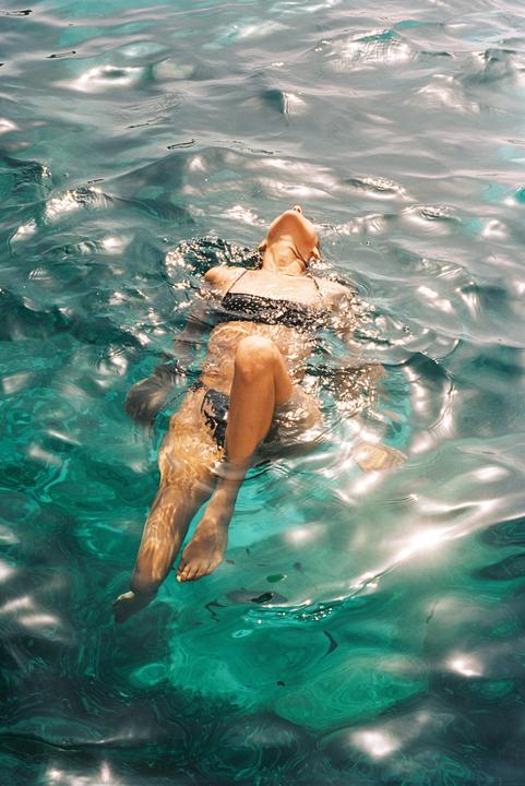 A woman floats on her back in clear turquoise water with sunlight reflecting on the surface.