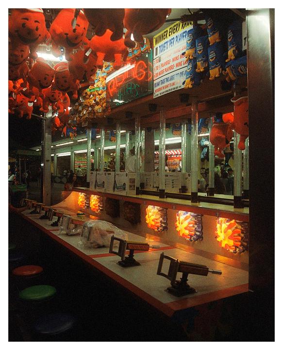 A carnival game booth is filled with stuffed animals and features toy guns for players to use.