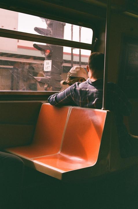 A couple sits on an orange seat in a vehicle, looking out the window at a traffic light.
