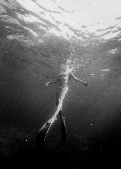 A woman wearing flippers swims underwater with light reflecting on the surface.