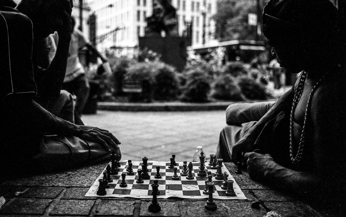 Two men play chess on a chessboard on a street.