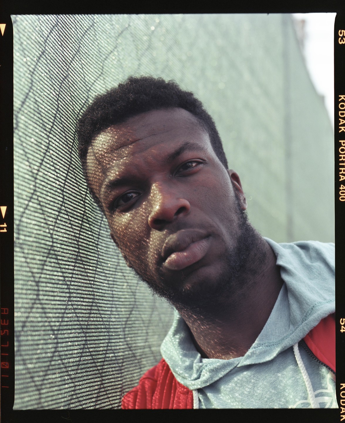A man with a beard and short hair leans against a fence.