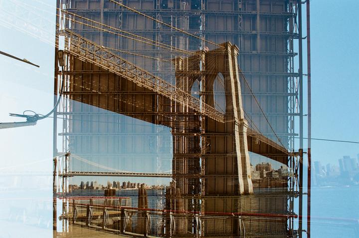 A double exposure shows the Brooklyn Bridge overlaid with a building under construction.