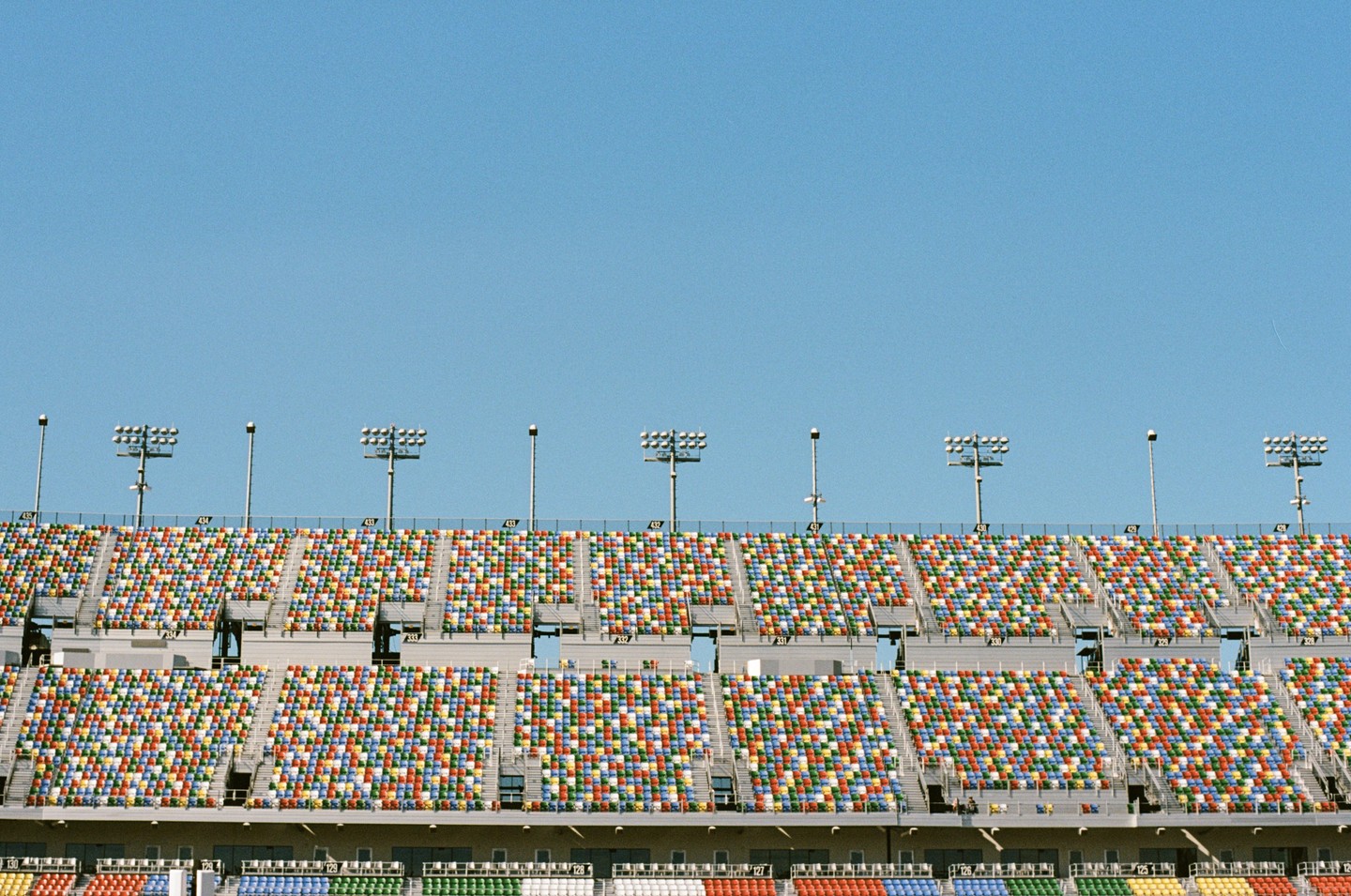 Empty stadium seating with multicolored chairs is visible under a clear blue sky.