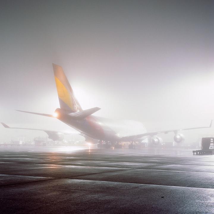 A large airplane is parked on an airfield in thick fog at night.