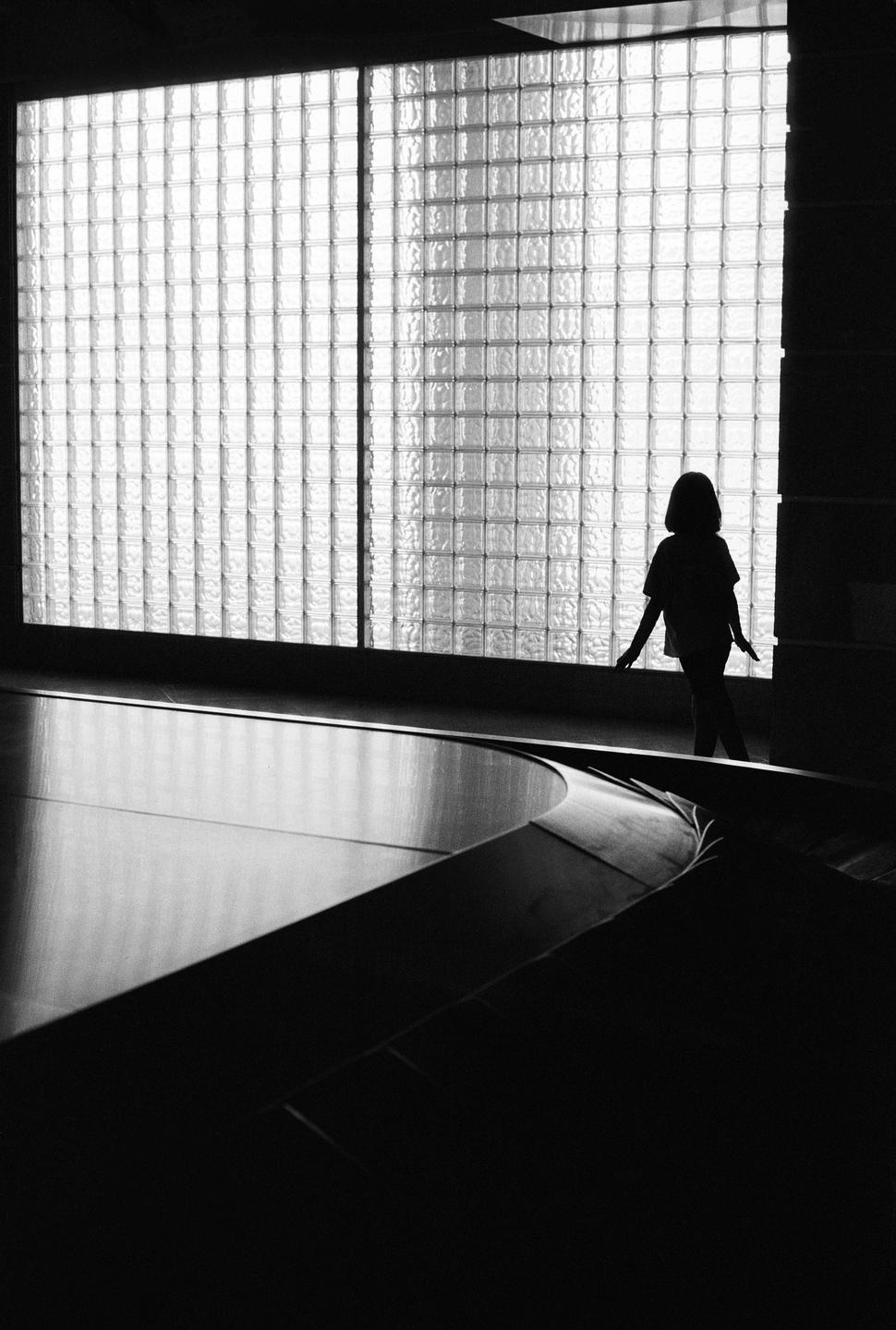 A child is silhouetted against a large window made of glass blocks.