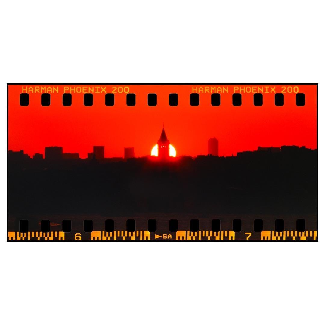 A bright red sunset silhouettes a city skyline with a prominent tower.