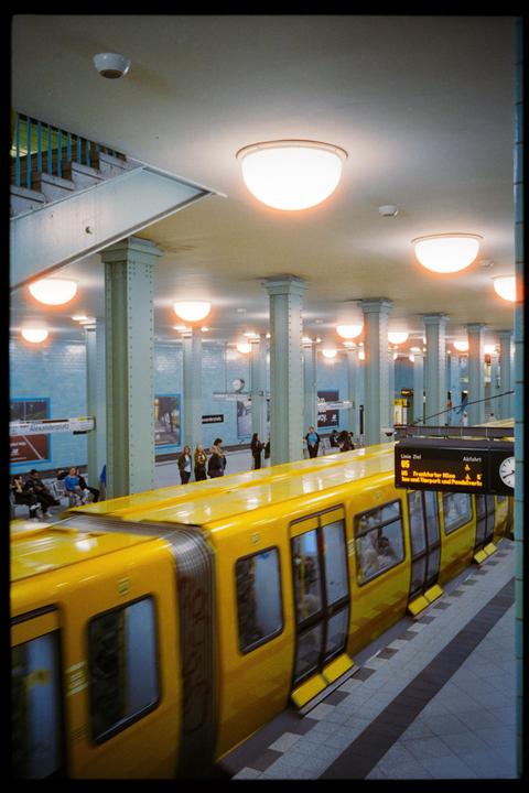 A yellow subway train is pulling into a station with people waiting on the platform.