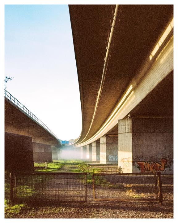 Two concrete overpasses curve over a grassy area with a metal fence and a hazy atmosphere.