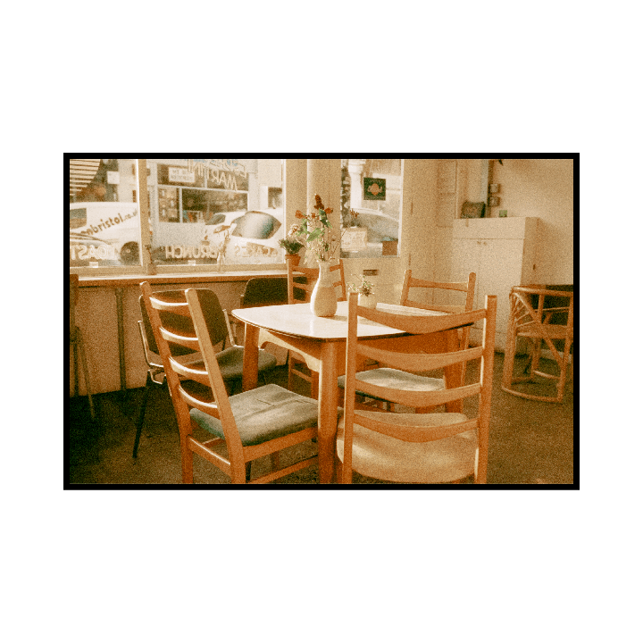 A cafe interior shows a table with chairs and a vase of flowers near a window.