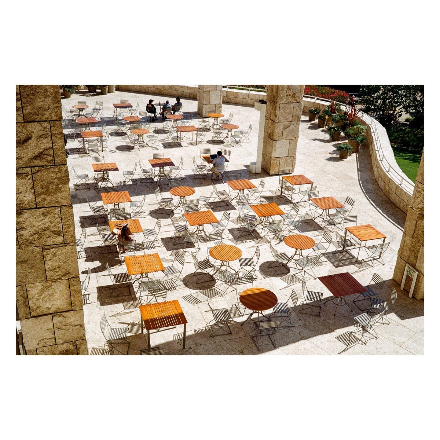 A high-angle view shows a patio with many tables and chairs, with a few people seated at some of them.