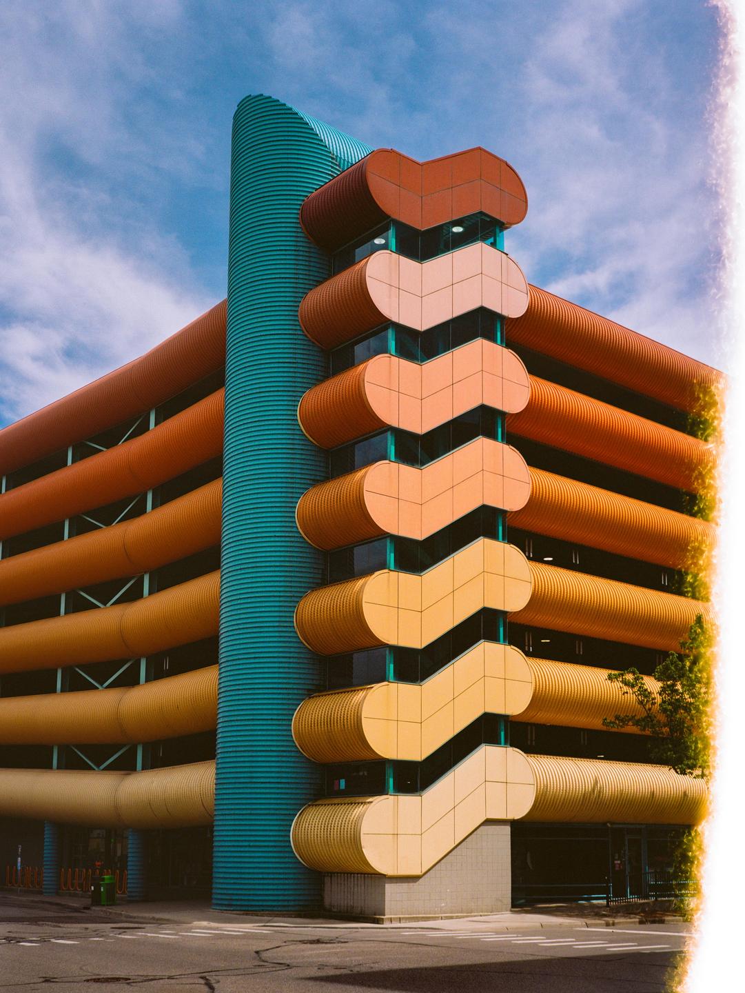 A colorful building with a teal column and orange and yellow levels is shown under a blue sky.