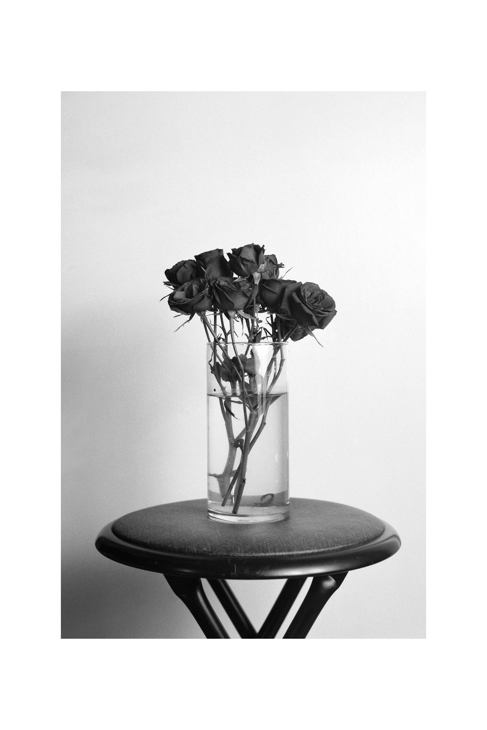 A bouquet of roses in a glass vase sits on a stool.