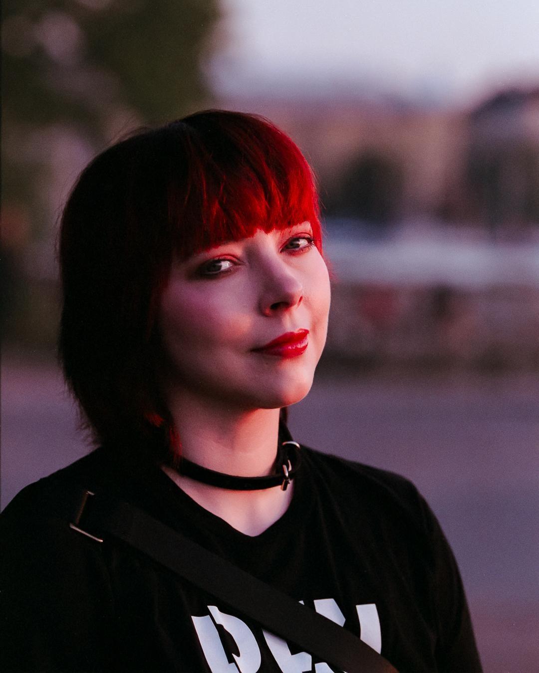 A woman with red hair and red lipstick looks at the viewer.