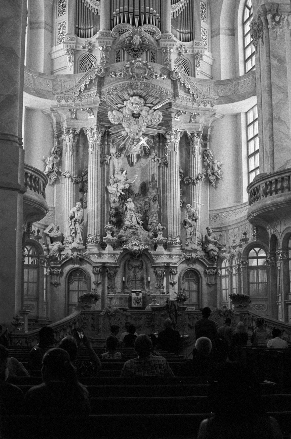A large ornate altar with an organ above it is visible behind the heads of people sitting in pews.