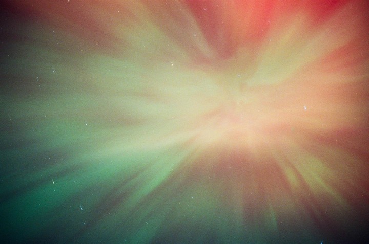 The aurora borealis glows green and red in the night sky, with small stars visible.