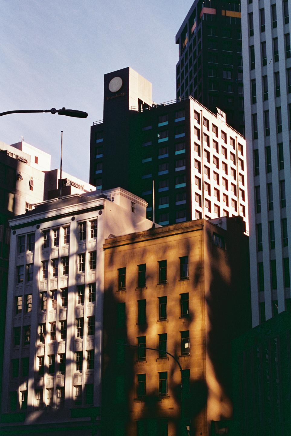 Sunlight and shadow play across the facades of several tall buildings in a city.