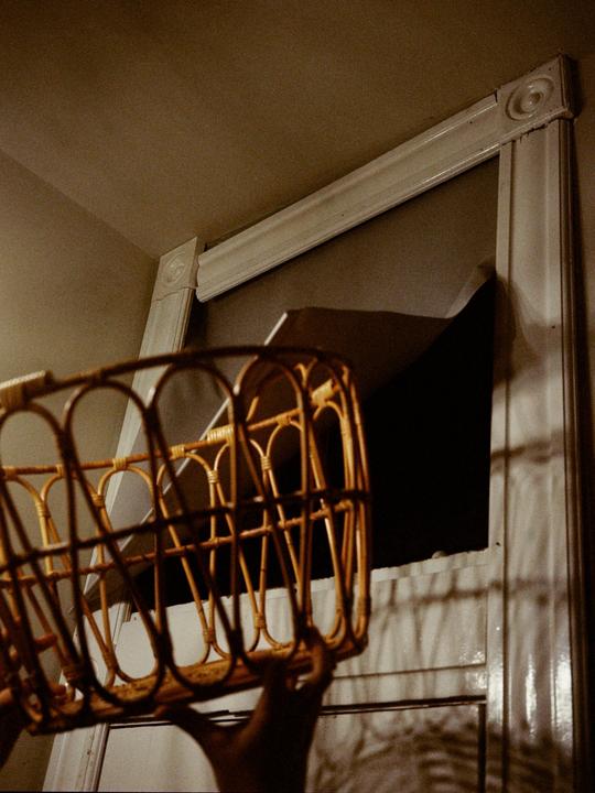 A hand holds a wicker basket in front of a window with a dark background.