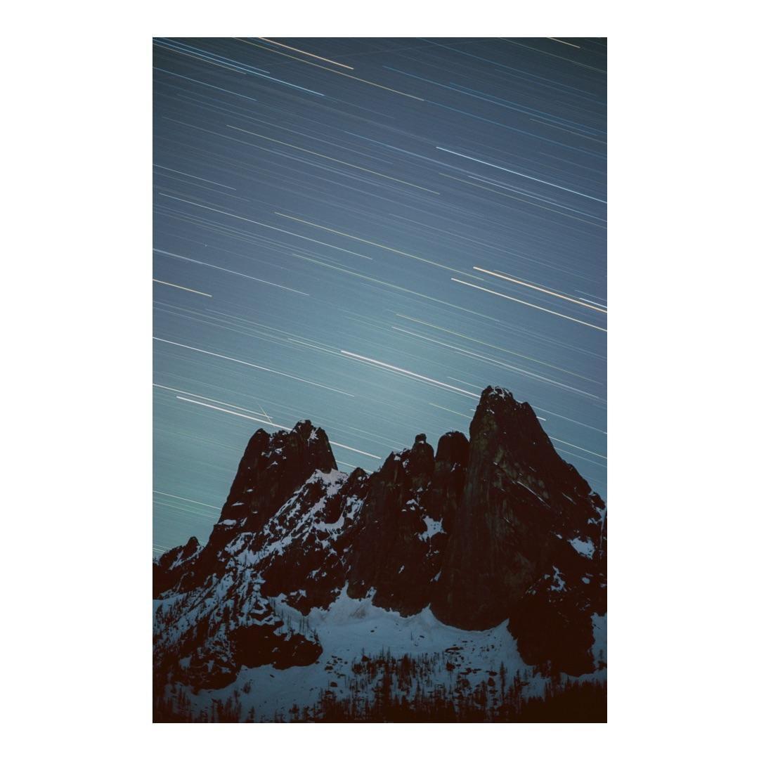 Snow-covered mountains are visible under a night sky with star trails.