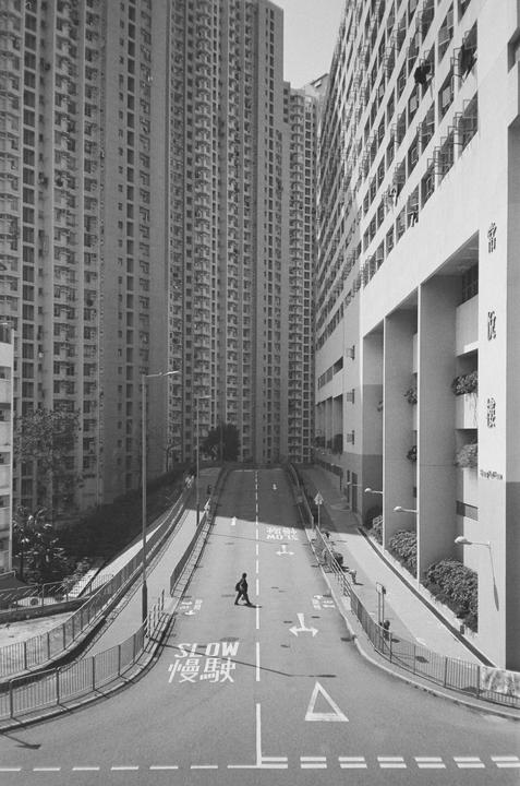 A person walks across a street between two tall buildings in Hong Kong.
