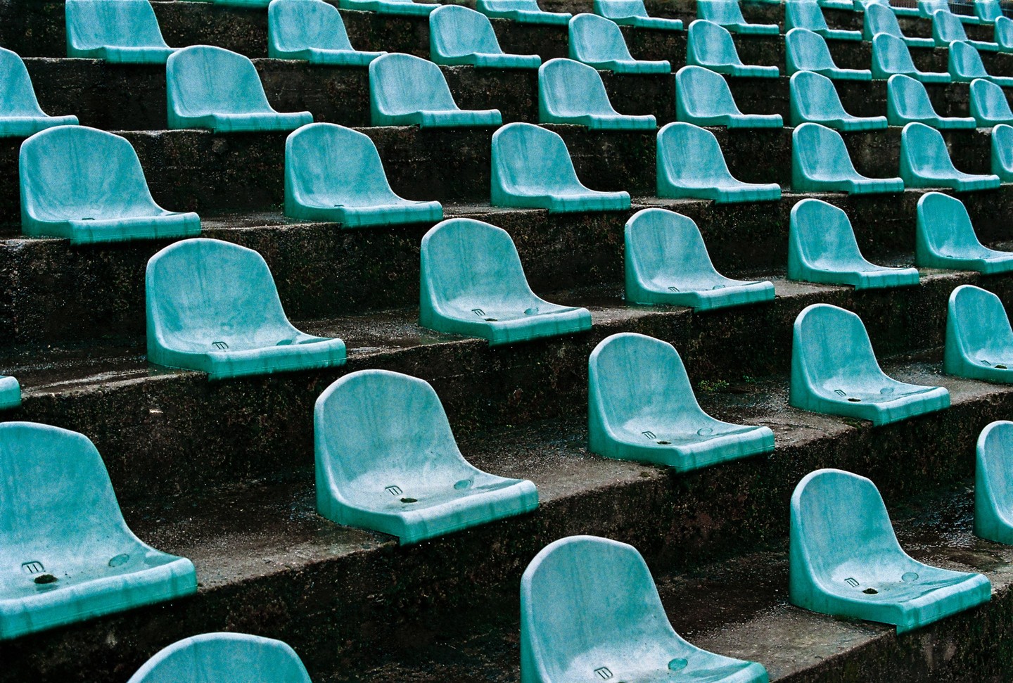 Rows of empty, dirty, light blue stadium seats are arranged on concrete steps.