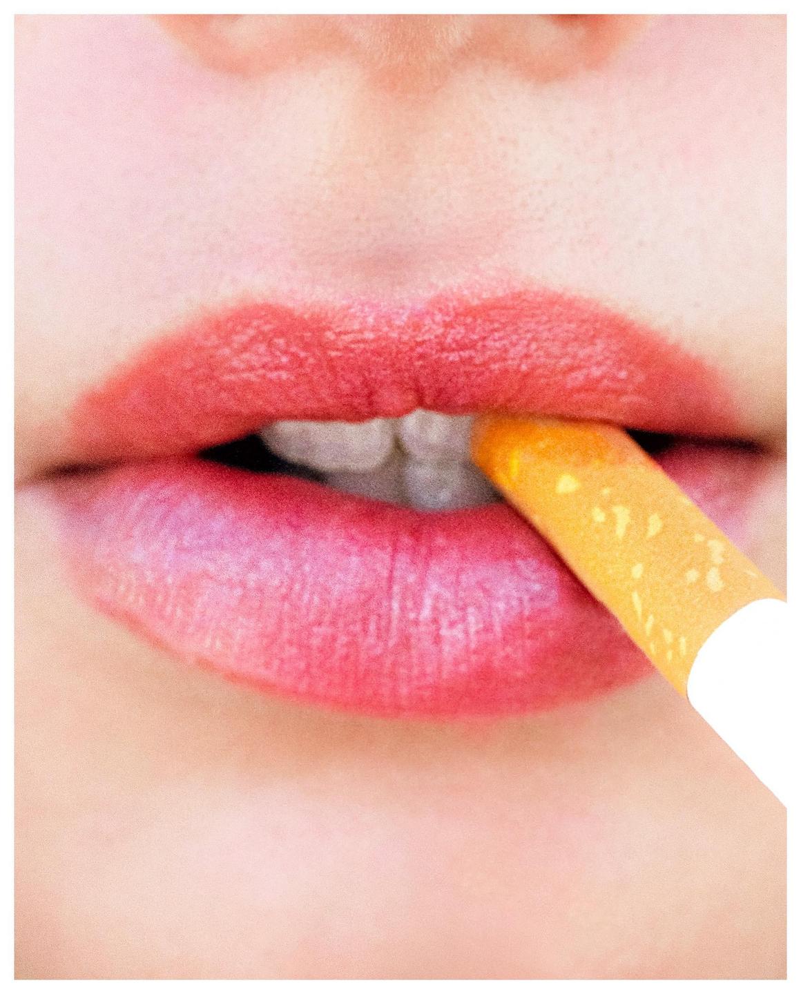 A woman's red lips hold a cigarette filter in her mouth.