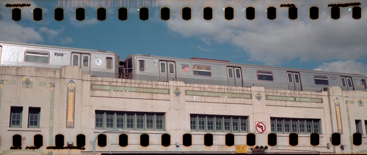 A subway train passes above a building with decorative tile work.