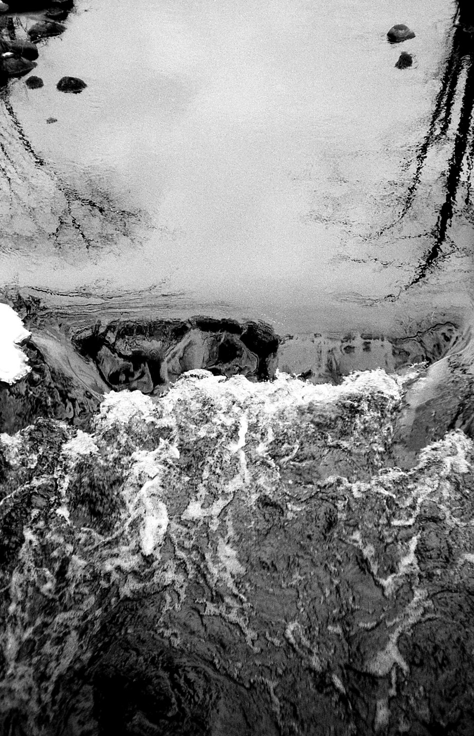 A body of water transitions from a calm surface with reflections to a turbulent, foamy cascade.