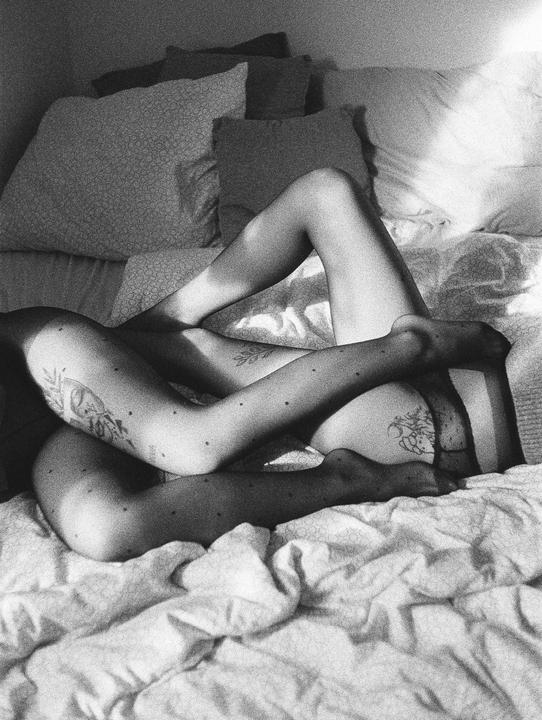 A woman's legs are entangled on a bed with pillows in the background.