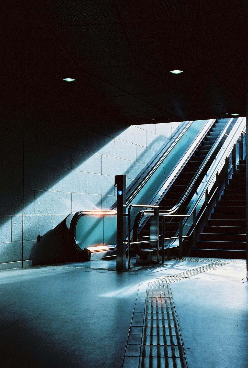 Sunlight illuminates an escalator and a staircase in a subway station.