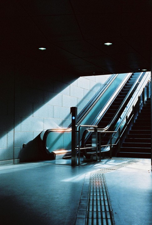 Sunlight illuminates an escalator and a staircase in a subway station.