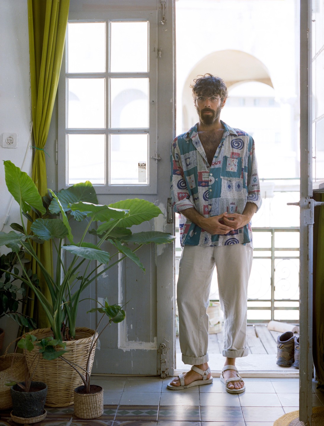 A man stands in a doorway with potted plants to his left.
