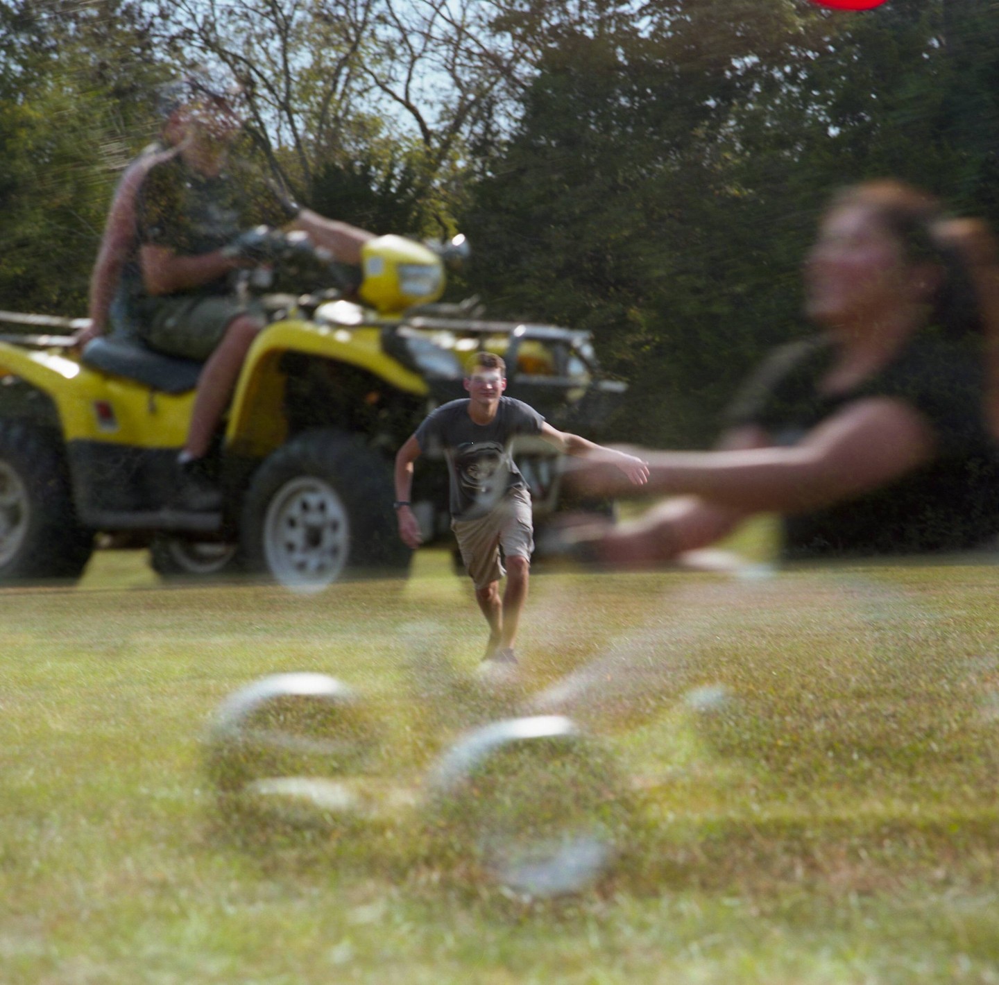 A man runs across a grassy field with a yellow ATV and another person in the background, all appearing in a double exposure.