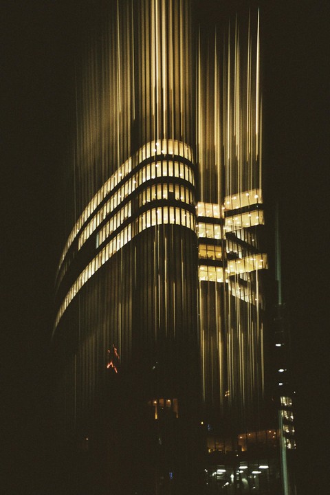 A tall building with illuminated windows is captured at night with light trails streaking upwards.