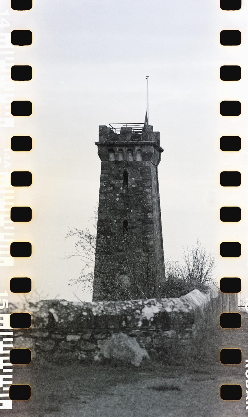 A stone tower with a flag on top stands behind a low stone wall.