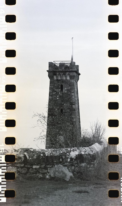 A stone tower with a flag on top stands behind a low stone wall.