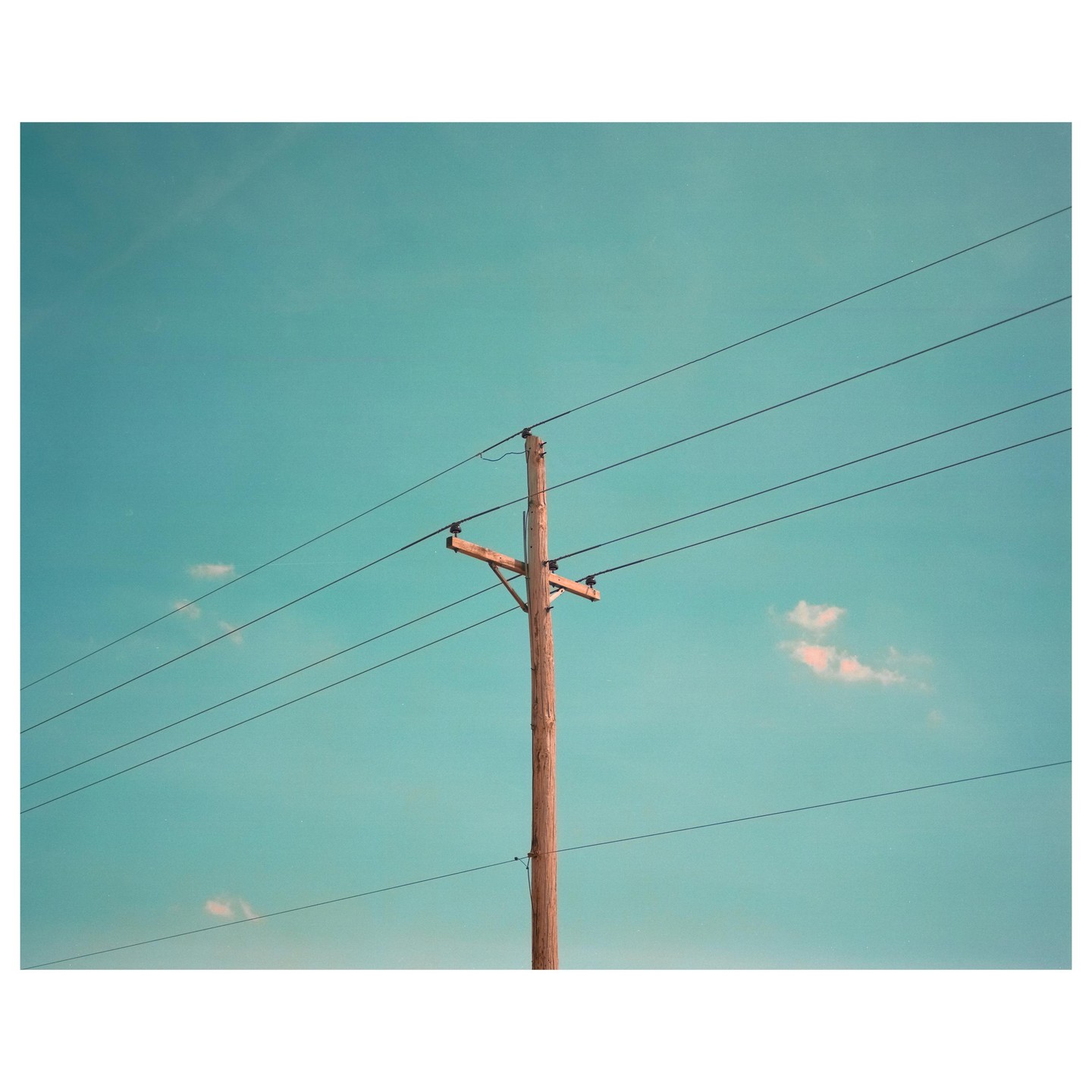 A wooden utility pole with wires stretches across a clear blue sky with a few small clouds.
