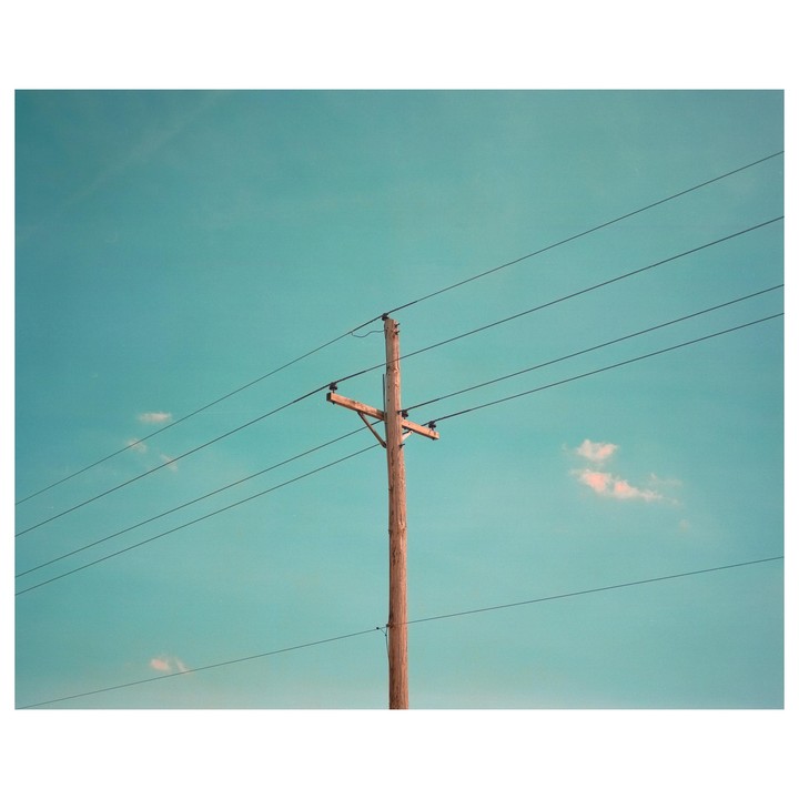 A wooden utility pole with wires stretches across a clear blue sky with a few small clouds.