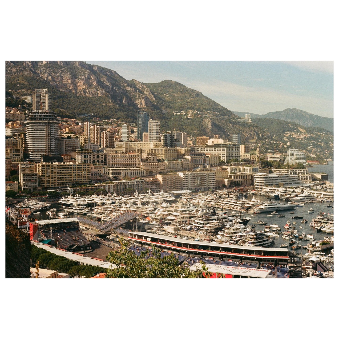 A panoramic view of Monaco shows a harbor filled with yachts, surrounded by buildings and mountains.