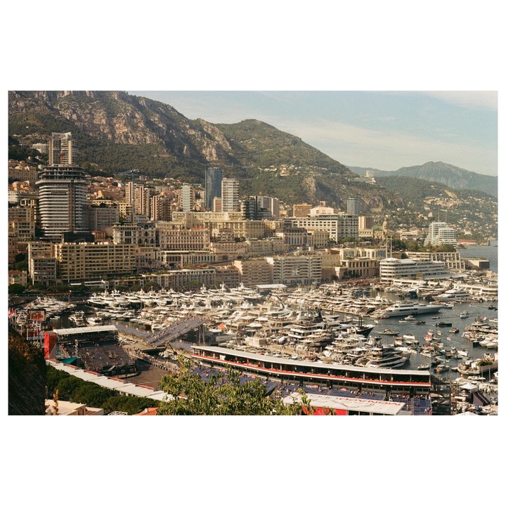 A panoramic view of Monaco shows a harbor filled with yachts, surrounded by buildings and mountains.