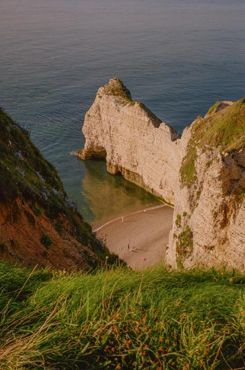 A high-angle view shows a beach nestled between two cliffs, with the ocean stretching out beyond.