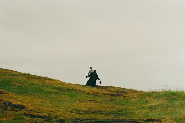 Two men are visible on a grassy hill under a bright sky.