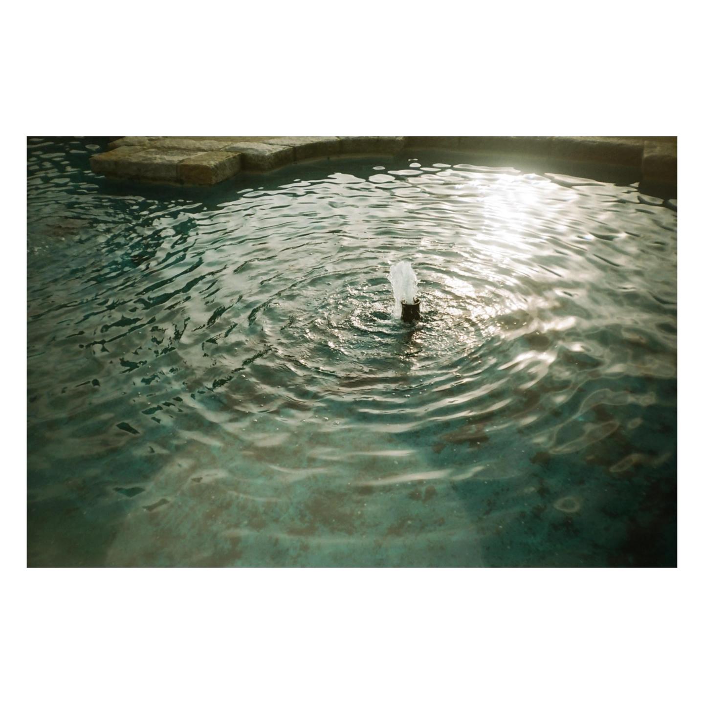 A small fountain sprays water in a pool with ripples on the surface.