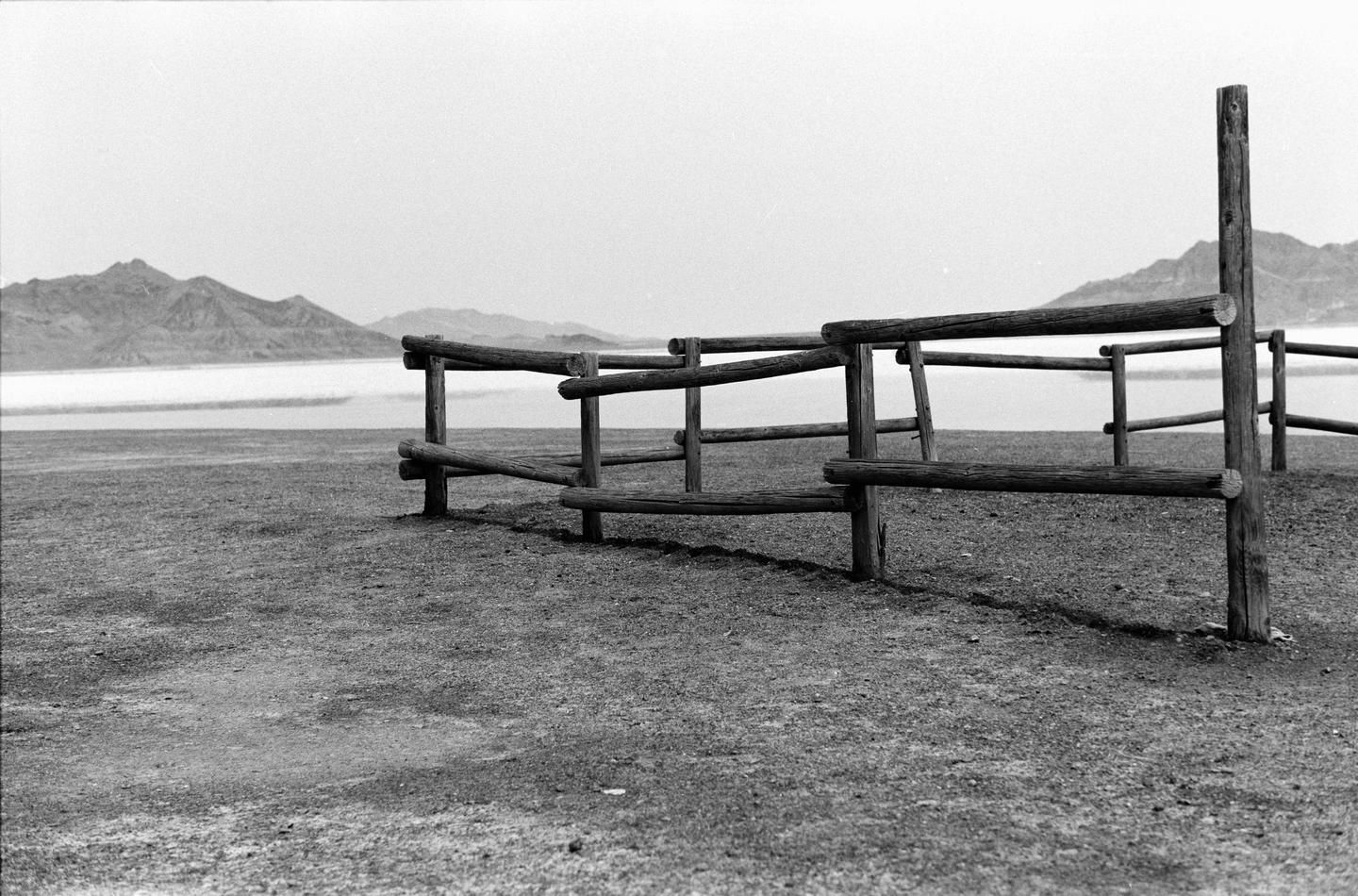 A wooden fence stands in the foreground with a body of water and mountains in the background.