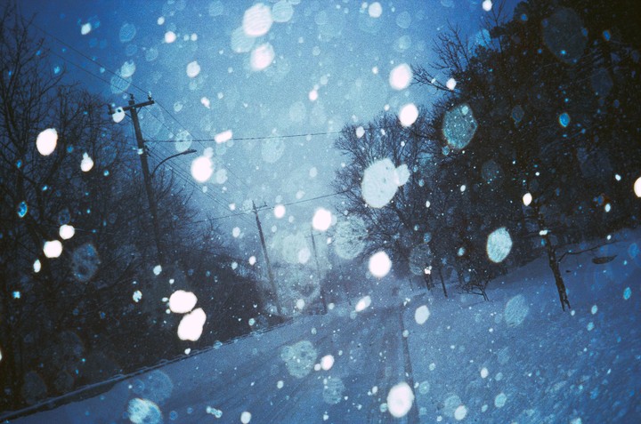 A snowy street with bare trees and utility poles is covered in large, bright bokeh.