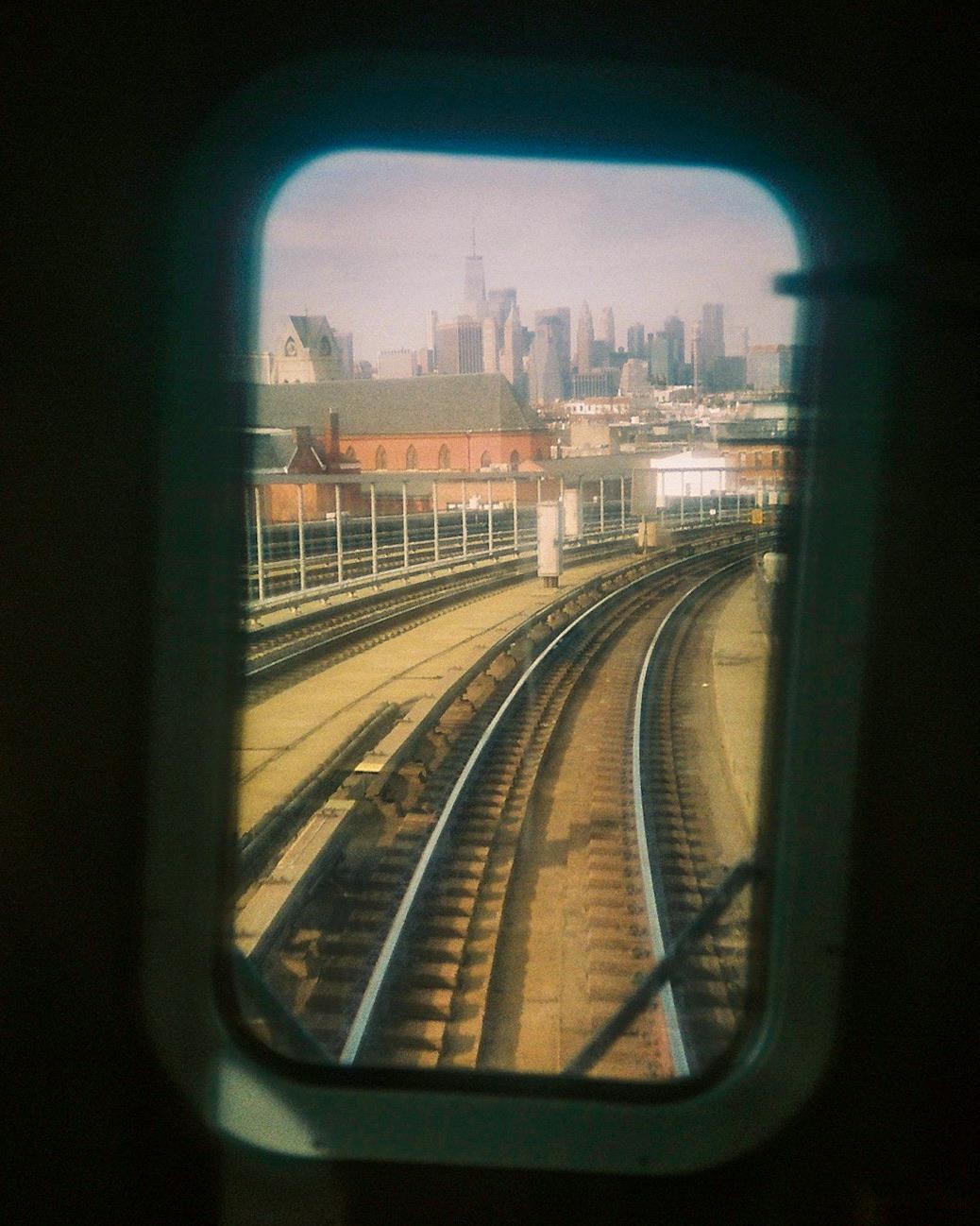 A view of train tracks curving towards a city skyline is seen through a train window.