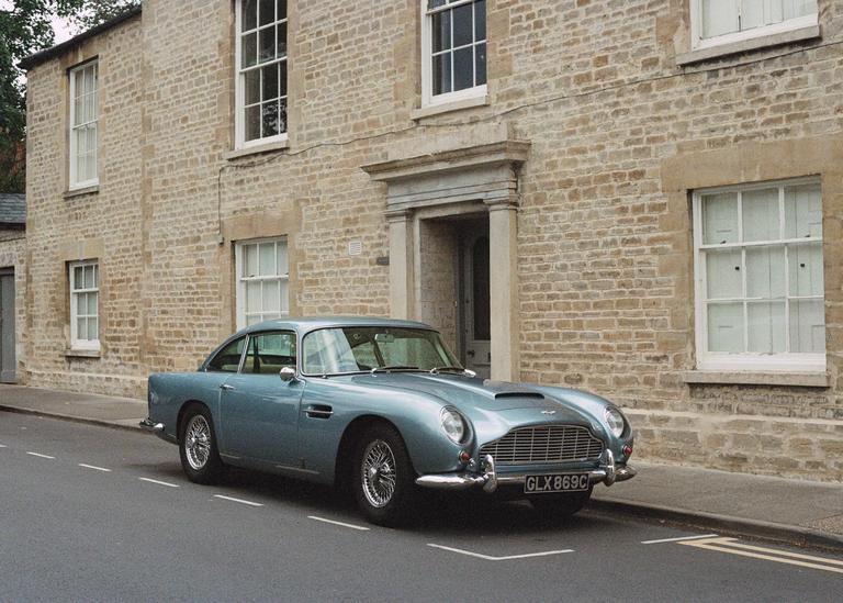 A blue vintage car is parked on a street in front of a stone building with white windows.