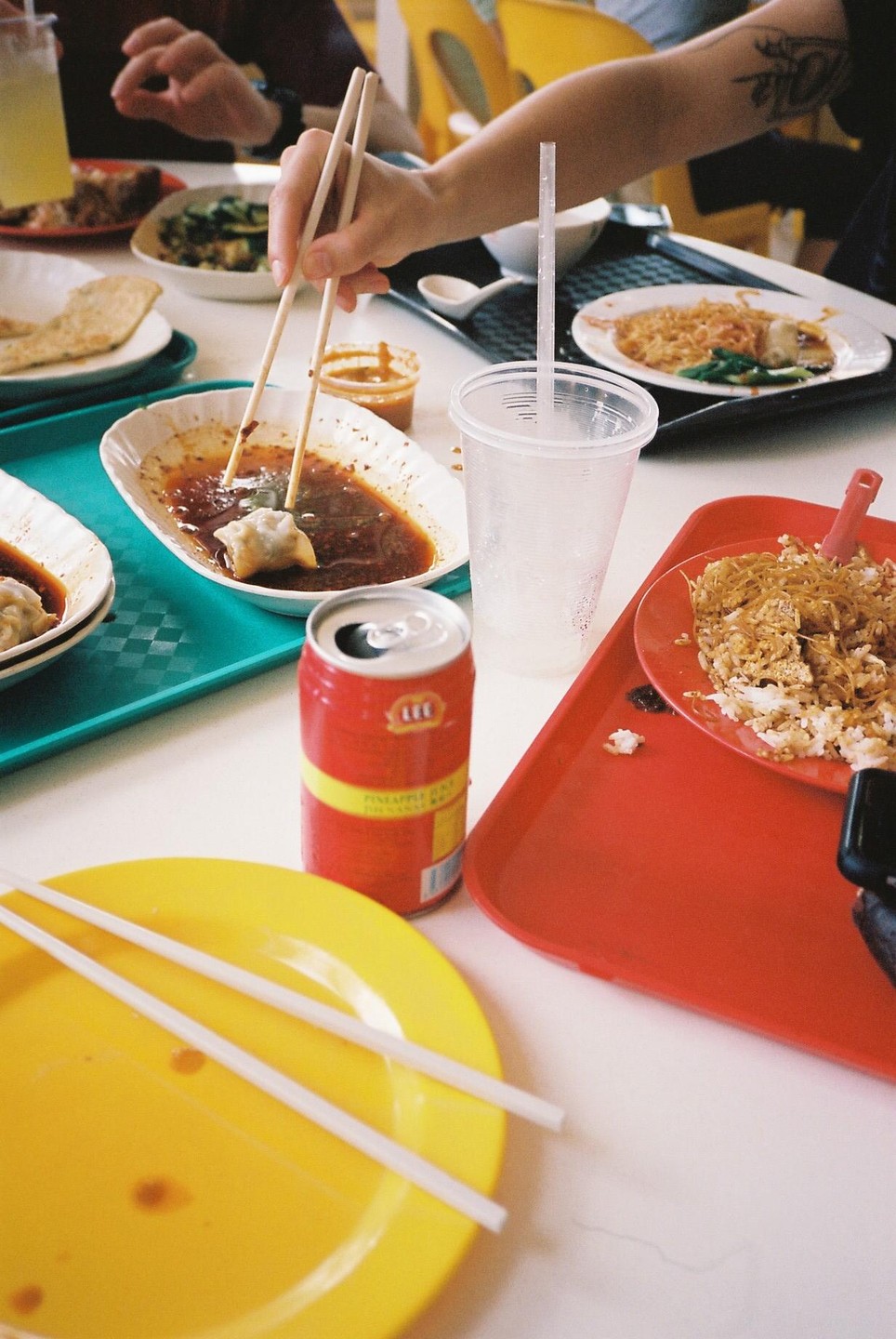 A person uses chopsticks to pick up a dumpling from a plate of sauce on a table with other food and drinks.