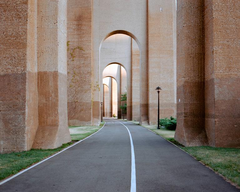 A paved path with a white line runs under a series of large concrete arches.
